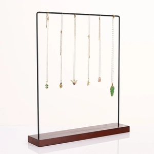 Minimalist metal jewelry stand with wooden base displaying several gold necklaces on white background
