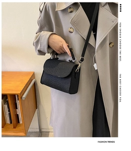 Detail of black crocodile embossed mini handbag styled with a beige trench coat