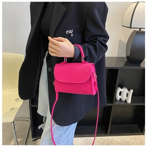 Detail of bright pink crocodile pattern square handbag held by a model in black suit