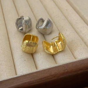 Close-up of textured huggie hoop earrings in gold and silver finish on corduroy