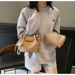 Detail of camel bucket bag with lychee texture, knot handle and pearl heart charm accessory