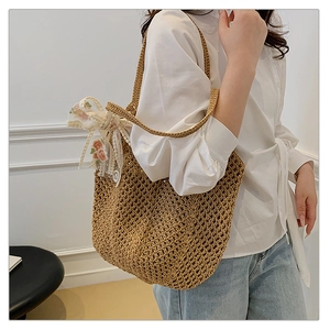Detail of hand-woven straw tote bag with floral ribbon shown on model shoulder