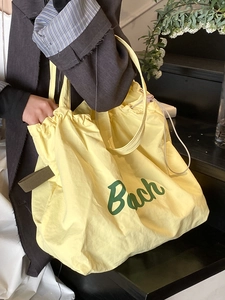 Light yellow oversized drawstring tote bag with green Bach lettering for travel