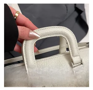 Detail view of thickened handles and lychee texture on a white leather handbag