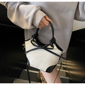 Sac seau bicolore chic avec texture crème et détail de nœud noir tenu par le modèle