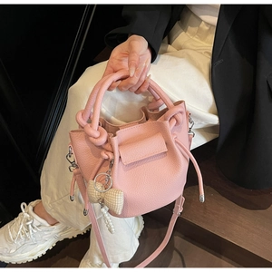 Detail of pink lychee leather bucket bag with knot handle and pearl ribbon charm