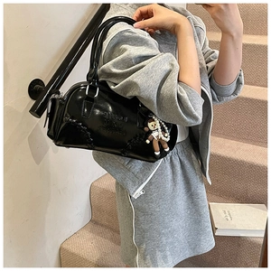 Detail of black glossy leather bowling bag with embossed logo and cute doll charm