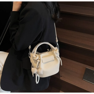 Detail of lychee pattern cream bucket bag with decorative bow and pearl charm