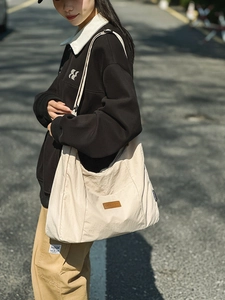 Detail of minimalist cream tote bag showing the brown leather logo and canvas texture