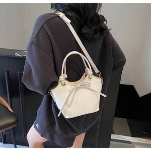 Détail du sac seau en cuir blanc crème avec poignée tressée et décoration de nœud élégant