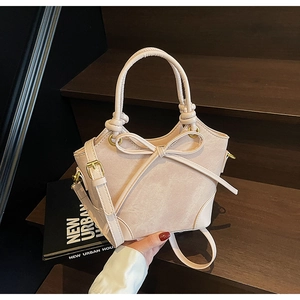 Détail d'un sac seau beige avec un grand nœud et une poignée décorative à nœuds