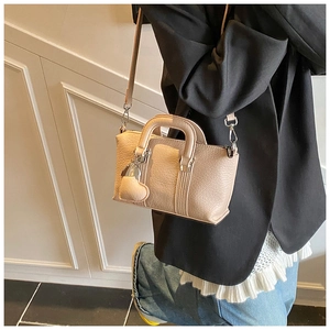 Detail showing litchi grain texture and heart-shaped charm on beige mini handbag