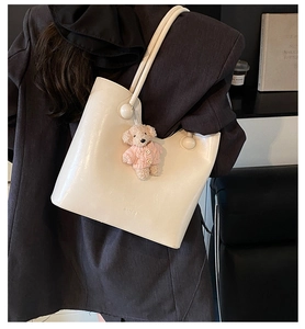 Detail of cream tote bag with round hardware and cute pink bear charm on grey suit