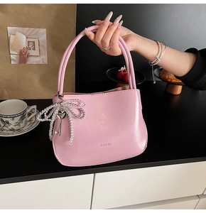 Detailed close-up of pink glossy bucket bag with pearl bow and heart metal charm