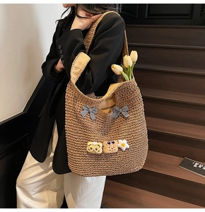 Detailansicht der braunen Strohtasche mit süßen Cartoon-Patches und karierten Schleifen