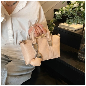 Chic beige crossbody bag with litchi texture and heart charm held by a model
