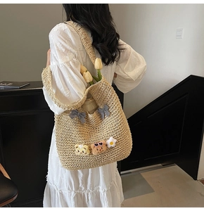 Detailaufnahme der Strohtasche mit karierter Schleife und Plüschbär am Modell getragen