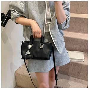Detail of black pebbled PU leather handbag with heart-shaped pendant and adjustable strap