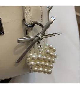 Dettaglio del fiocco argento e ciondolo a cuore di perle su una borsa in pelle bianca