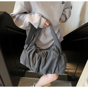 Bolso nube plisado gris oscuro con correa ancha llevado por una modelo en un estilo minimalista