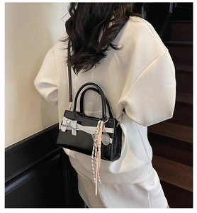 Borsa a tracolla nera alla moda con fiocco bianco e ciondolo a racchetta indossata dalla modella