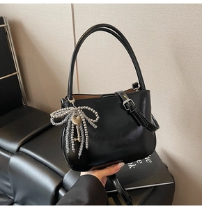 Detail of black PU bucket bag featuring a silver beaded bow charm and key pendant