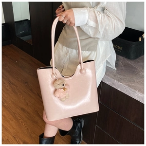 Detail of light pink faux leather tote bag with cute bear charm and slim straps