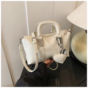 Detailed macro view of cream-white pebbled leather handbag with silver hardware and heart charm