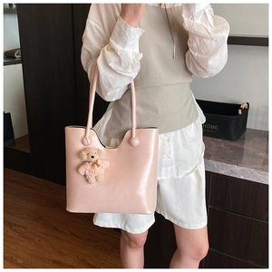 Close-up of pink patent leather tote bag with long strap and cute plush bear charm accessory