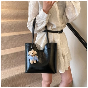 Detail of black glossy leather bucket bag with a cute brown teddy bear charm