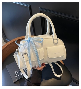 Detail of white Boston bag featuring textured leather, front pockets, and a lace ribbon