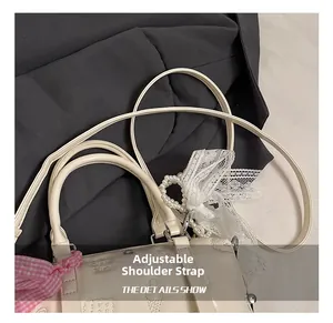 Detail of adjustable shoulder strap with elegant pearl and lace bow charms on a cream bag