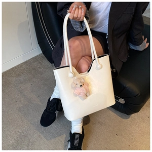 Detail of a creamy white PU leather bucket bag with a cute pink sweater teddy bear charm