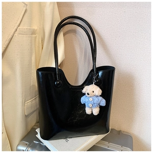 Detail of black glossy leather bucket bag with a cute teddy bear charm and brand logo
