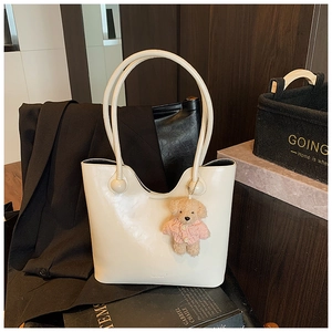 Detail of a creamy tote bag featuring a cute teddy bear charm and unique ball handle design