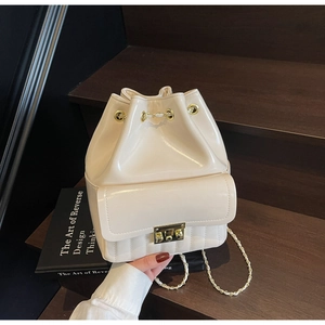 Dettaglio borsa a secchiello beige con chiusura dorata e tracolla a catena su scale