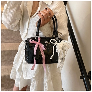 Detail of black Boston bag featuring pink lace bow and white pearl chain accessories