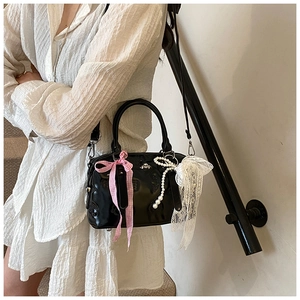 Close-up of black glossy pillow bag with lace, pink plaid bow and pearl pendants