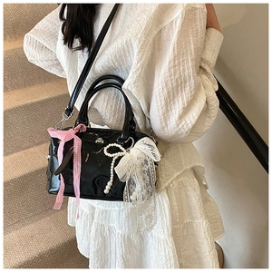 Detail of black patent leather Boston bag with pink ribbon bows and pearl charm