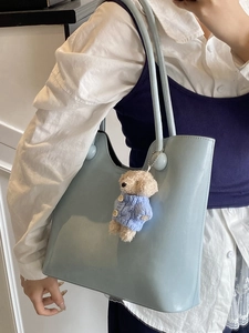 Light blue minimalist tote bag with teddy bear charm shown on a female shoulder