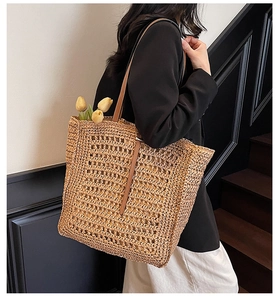 Detail of handwoven straw tote bag with brown leather straps and floral accent