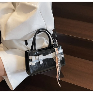 Dettaglio di borsa nera lucida con fiocco bianco e accessorio nappa in corda colorata