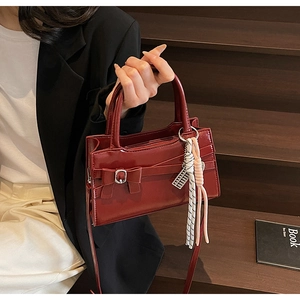 Dettaglio della borsa in pelle lucida bordeaux con fiocco e ciondoli metallici intrecciati
