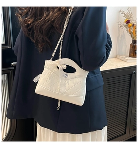 Detail of white quilted handbag featuring a delicate lace bow and silver twist lock