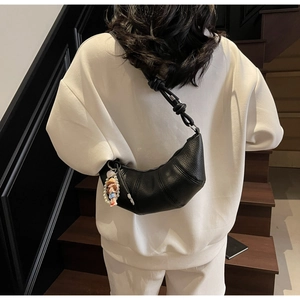 Détail du sac croissant noir avec bandoulière nouée et breloque poupée en perles
