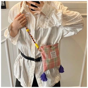 Detail of pink and green plaid crossbody bag with colorful woven strap and purple tassels