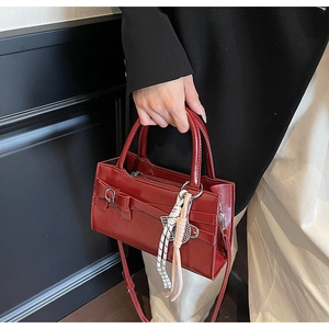 Dettaglio borsa bordeaux lucida con fiocco decorativo e ciondolo tenuta a mano