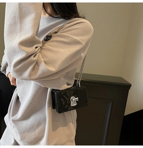 Detail of black snake-skin texture bag with silver lock clasp on waffle knit outfit