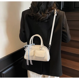 Detail of a beige Boston bag with ribbon bow and dual front pockets worn on a shoulder