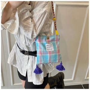 Detail of blue and pink plaid canvas crossbody bag with purple fringe and woven strap